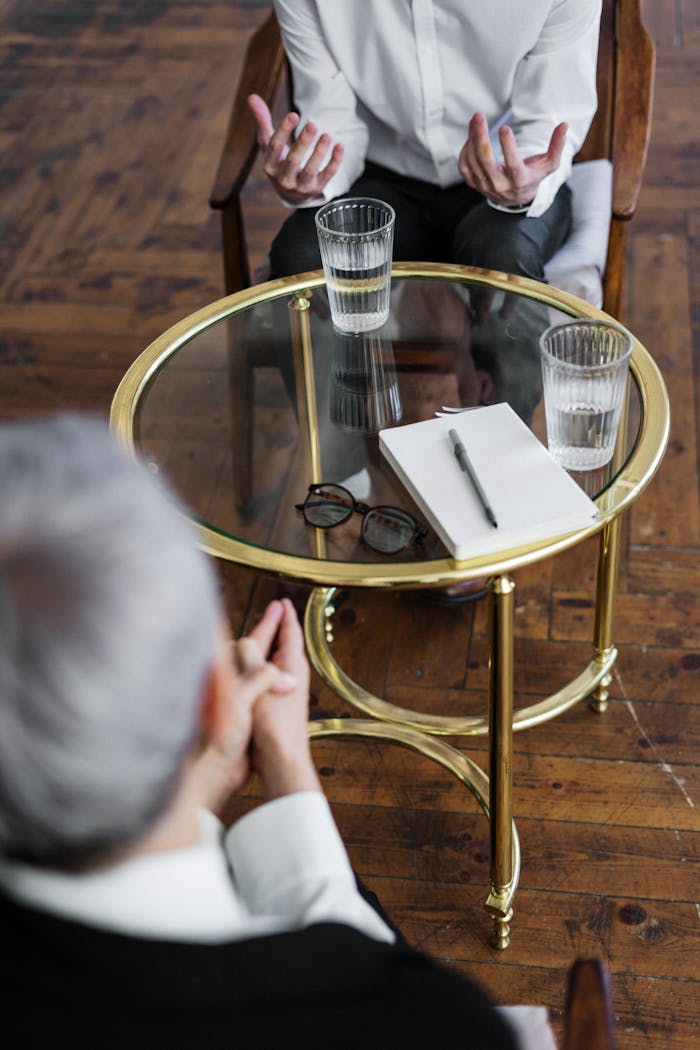 Services-03 Two adults discussing mental health in a counseling session across a glass table indoors.